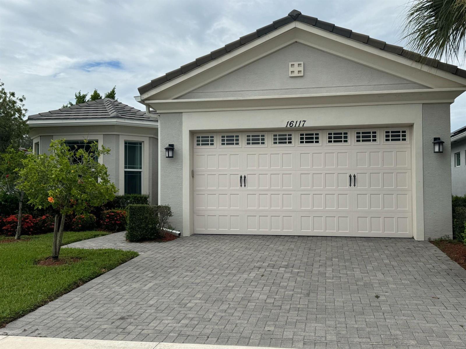 A single-story house exterior features a two-car garage, a paved driveway, and a small tree — 16117 Whippoorwill Circle, FL 33470, FL