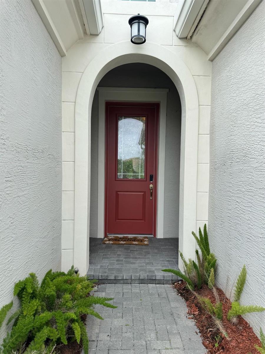 A red front door is framed by an arched entryway with a stone-paved walkway — 16117 Whippoorwill Circle, FL 33470, FL