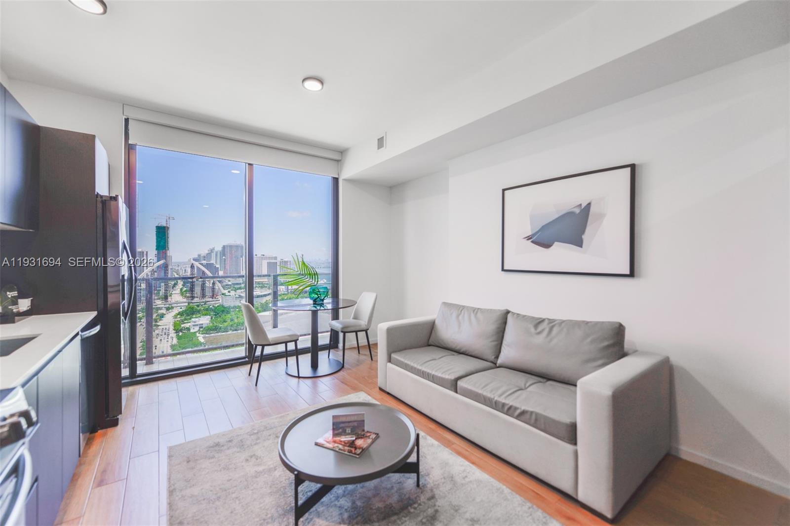 A modern living room features a grey sofa, circular coffee table, and floor-to-ceiling city views — 398 NE 5th St # 2407, Miami FL 33132, MIAMI, FL