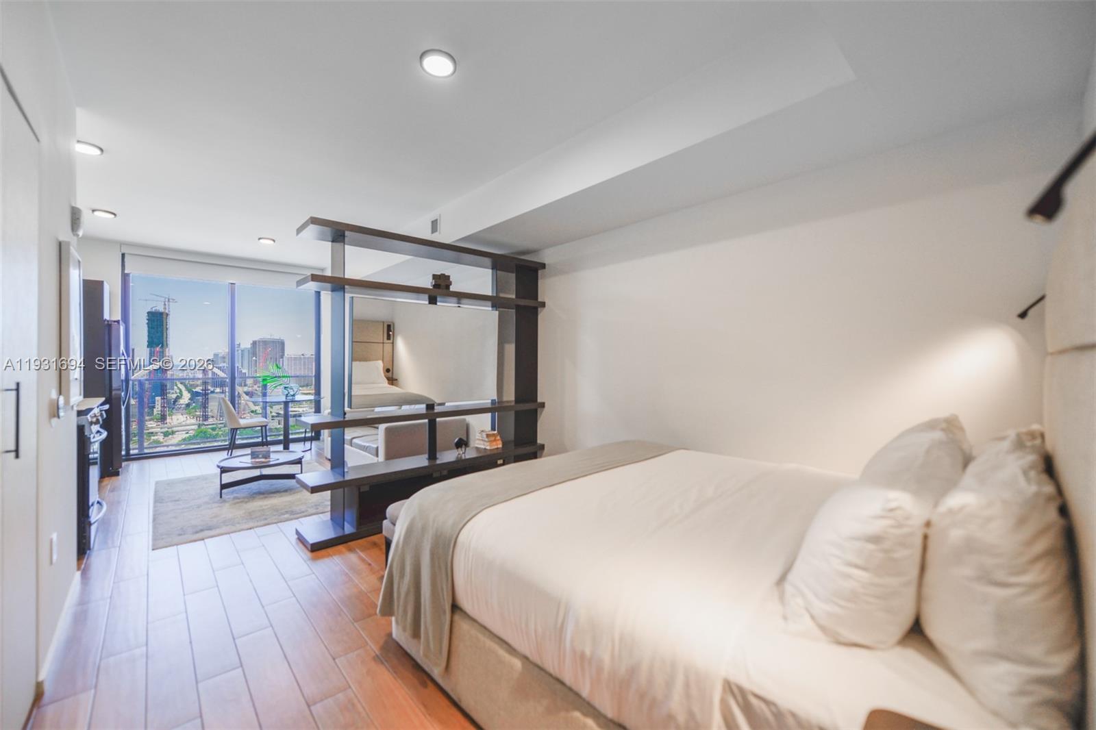 A modern studio apartment features a bed, a room divider, and floor-to-ceiling windows with views — 398 NE 5th St # 2407, Miami FL 33132, MIAMI, FL