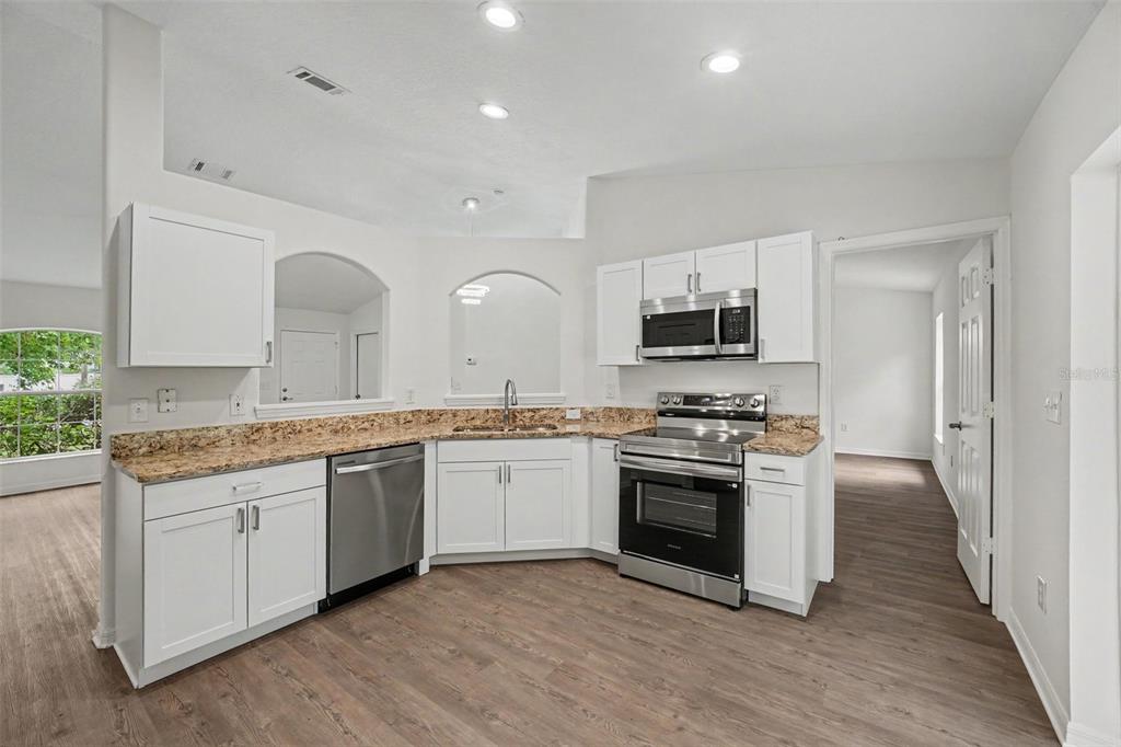 A kitchen with white cabinets, granite countertops, stainless steel appliances, and wood-look flooring — 30 PIERMOUNT LANE, PALM COAST, FL