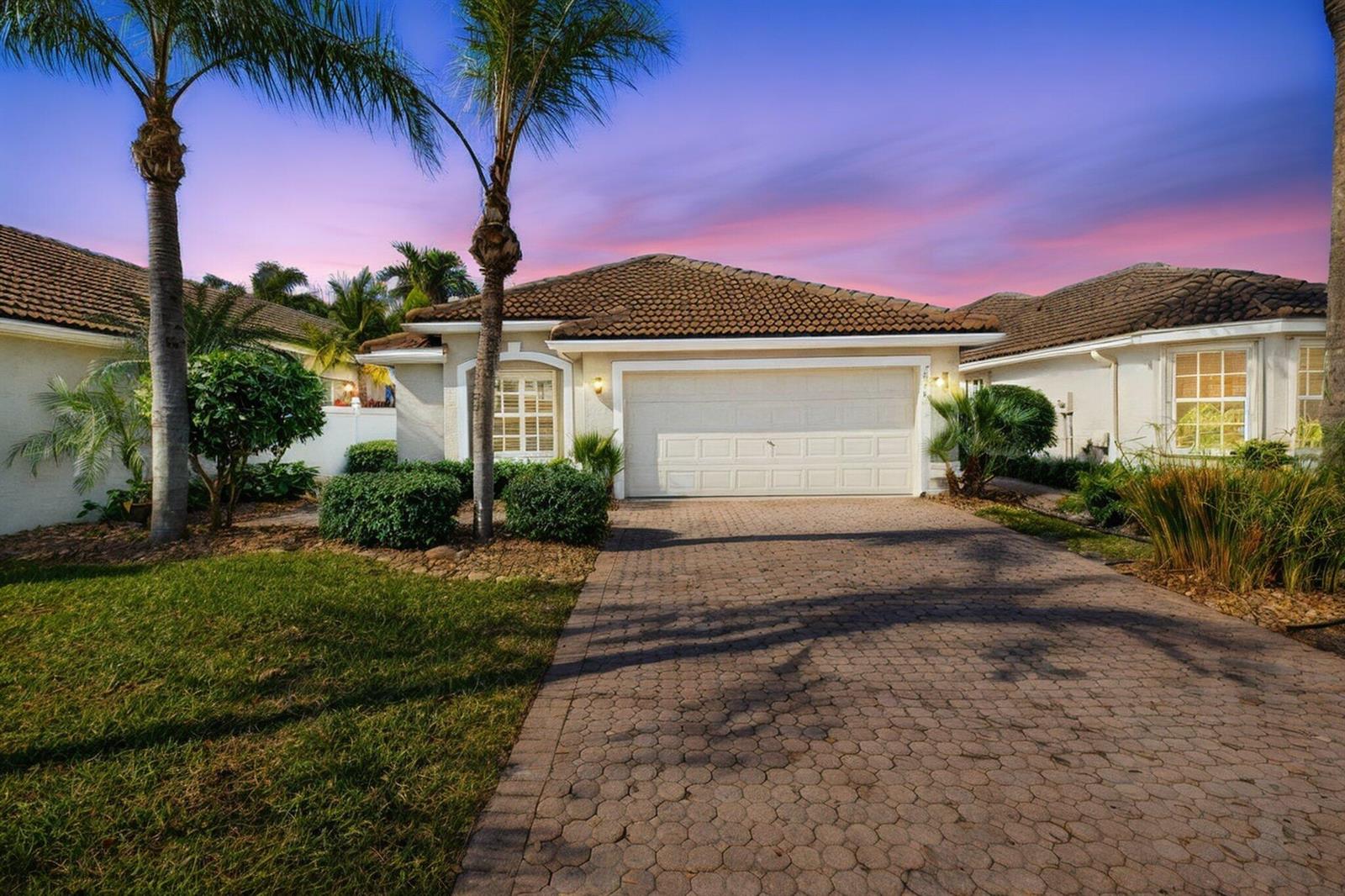 A single-story house with a paved driveway, a two-car garage, and palm trees at sunset — 7440 W Mercada Way, Delray Beach FL 33446, DELRAY BEACH, FL