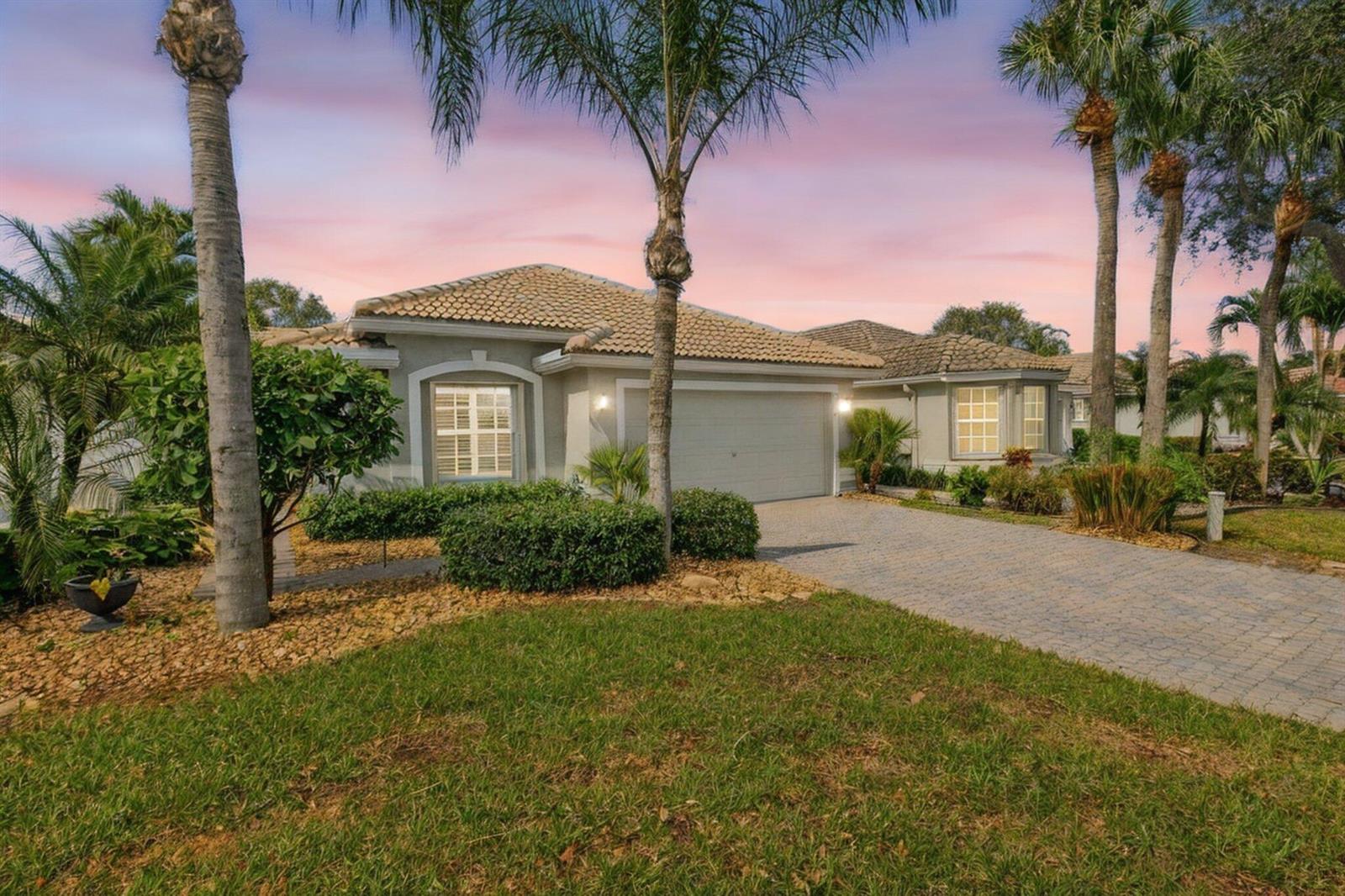 A single-story house with a paved driveway, a two-car garage, and palm trees at sunset — 7440 W Mercada Way, Delray Beach FL 33446, DELRAY BEACH, FL