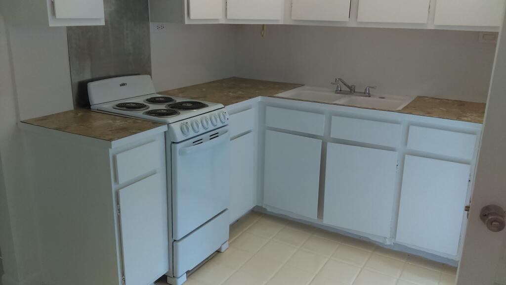 A small kitchen features white cabinets, a white electric stove, and tan laminate countertops — 11810 Ellison Wilson Road, FL 33408, FL