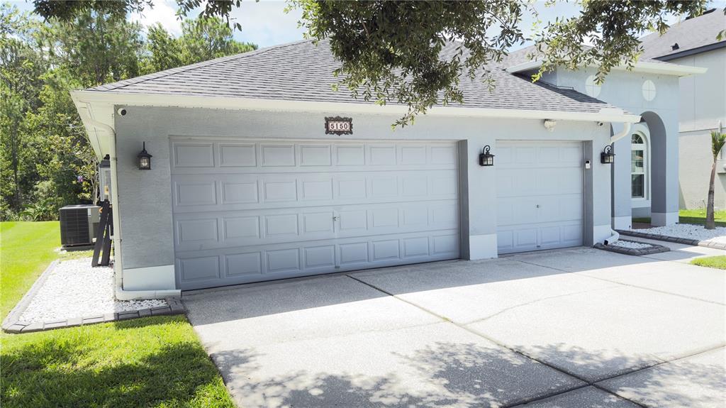 A single-story house with a three-car garage and a concrete driveway under a tree — 5150 VILLAGEBROOK DRIVE, WESLEY CHAPEL, FL