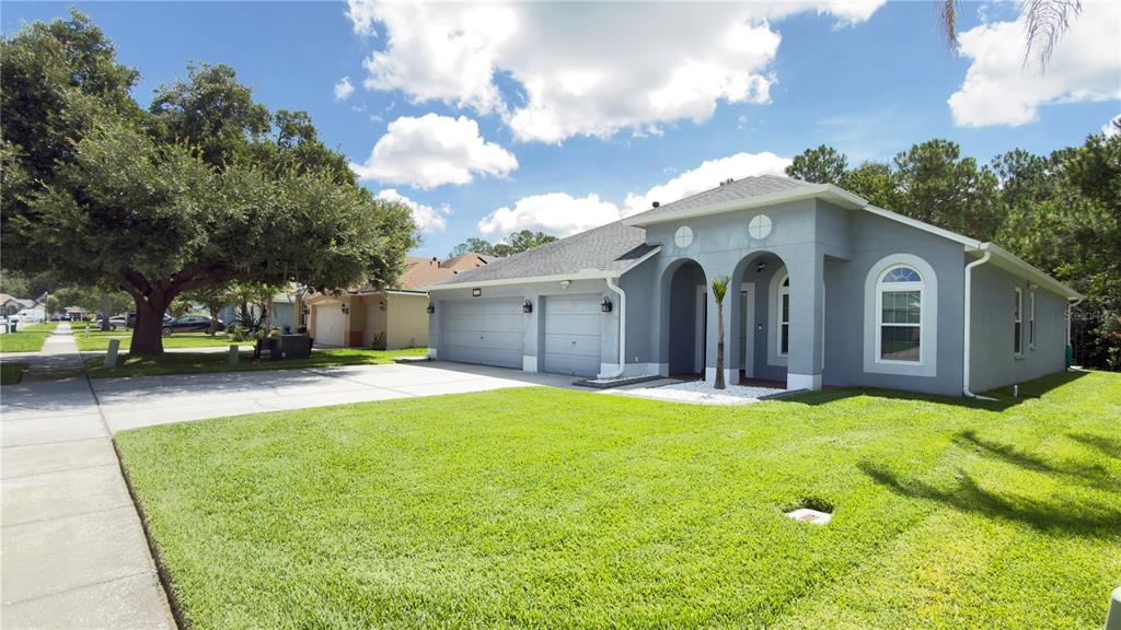 A gray house exterior features a blue front door under two arched entryways — 5150 VILLAGEBROOK DRIVE, WESLEY CHAPEL, FL