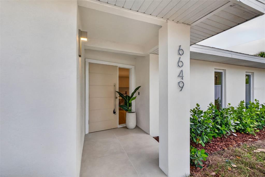 A modern front entrance features a light-colored door, a potted plant, and vertical house numbers — 6649 PINELLAS POINT DRIVE S, ST PETERSBURG, FL
