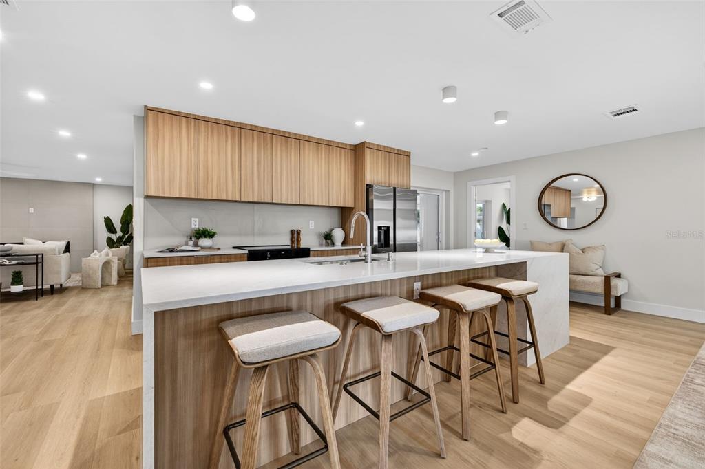 A modern kitchen features light wood cabinetry, a white waterfall island, and three bar stools — 6649 PINELLAS POINT DRIVE S, ST PETERSBURG, FL