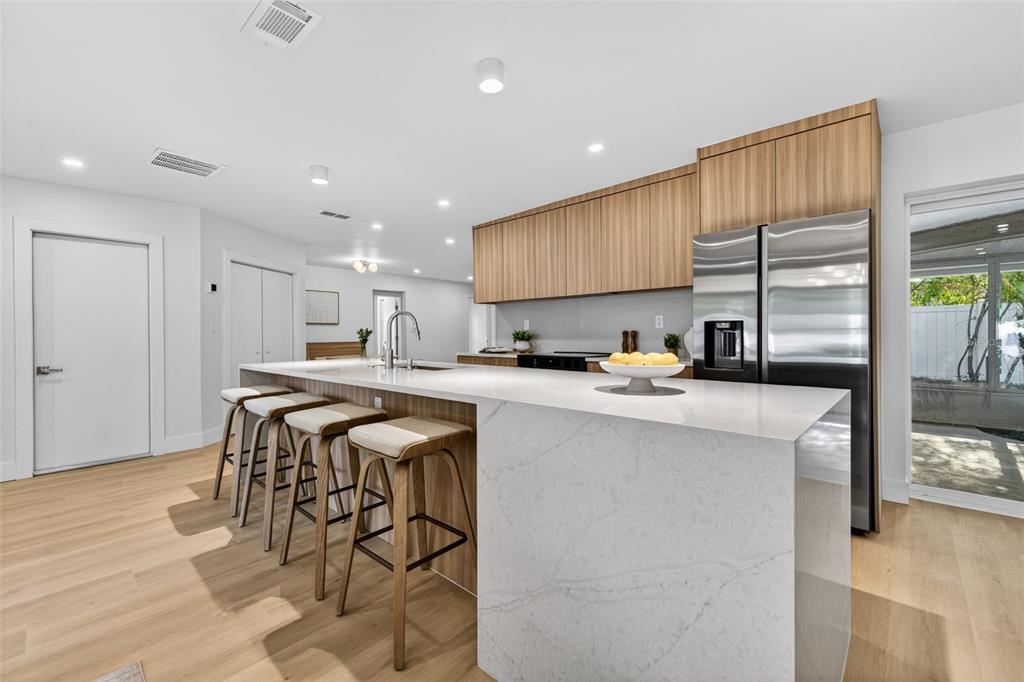 A modern kitchen features a large white quartz island, wood cabinetry, and light wood flooring — 6649 PINELLAS POINT DRIVE S, ST PETERSBURG, FL