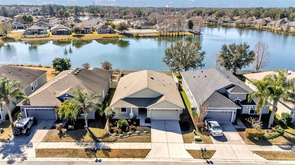 An aerial view shows three suburban houses with driveways facing a lake — 2447 LADOGA DRIVE, LAKELAND, FL