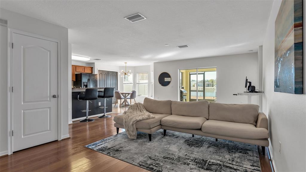 An open-concept living room features a sectional sofa, hardwood floors, and an adjacent kitchen area — 2447 LADOGA DRIVE, LAKELAND, FL
