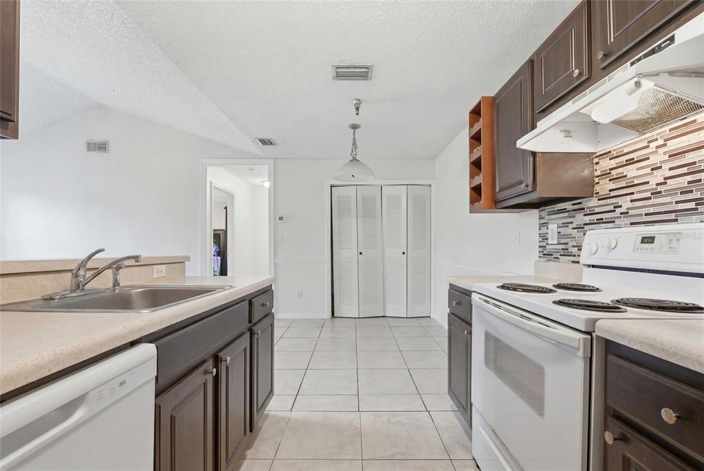 A kitchen features dark wood cabinets, light countertops, white appliances, and a tiled floor — 10265 GANDY BOULEVARD N UNIT 1806, ST PETERSBURG, FL