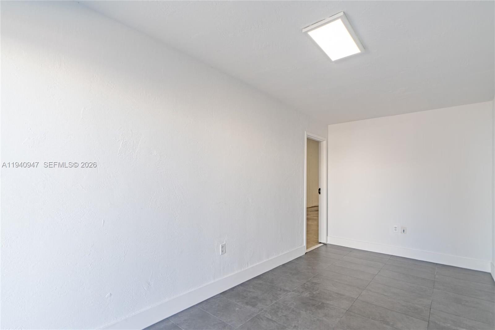 An empty room features white walls, gray tile flooring, and a rectangular ceiling light — 1676 W 31st Pl, Hialeah FL 33012, HIALEAH, FL
