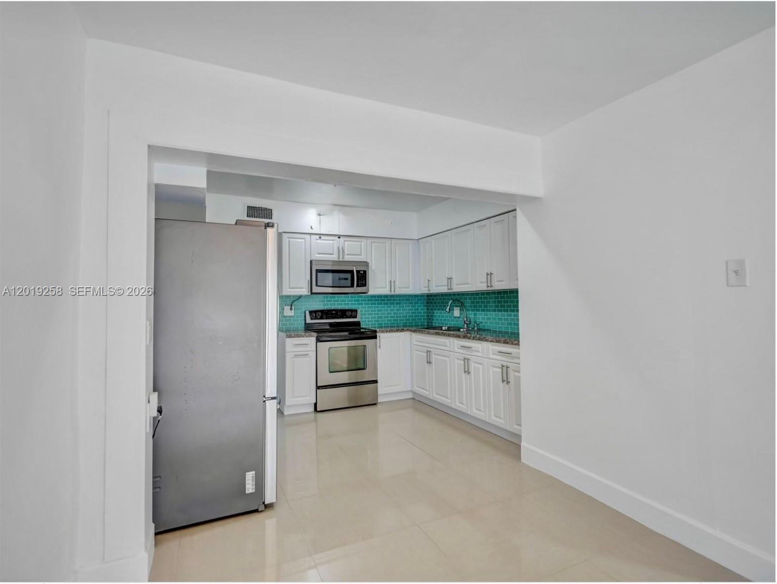 A kitchen features white cabinets, stainless steel appliances, and a teal tiled backsplash — 9494 SW 39th St, Miami FL 33165, MIAMI, FL