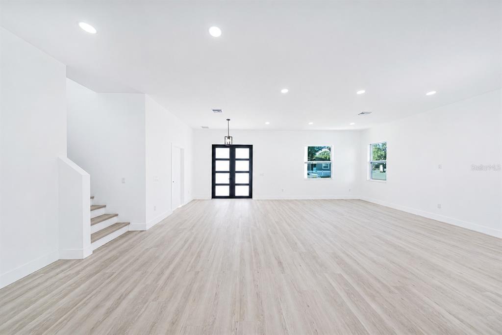 A bright, open-concept living area features light wood-look flooring, white walls, and a staircase — 2925 13TH STREET N, ST PETERSBURG, FL