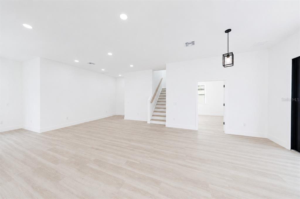 An open-concept room features white walls, light wood-look flooring, recessed lighting, and a staircase — 2925 13TH STREET N, ST PETERSBURG, FL