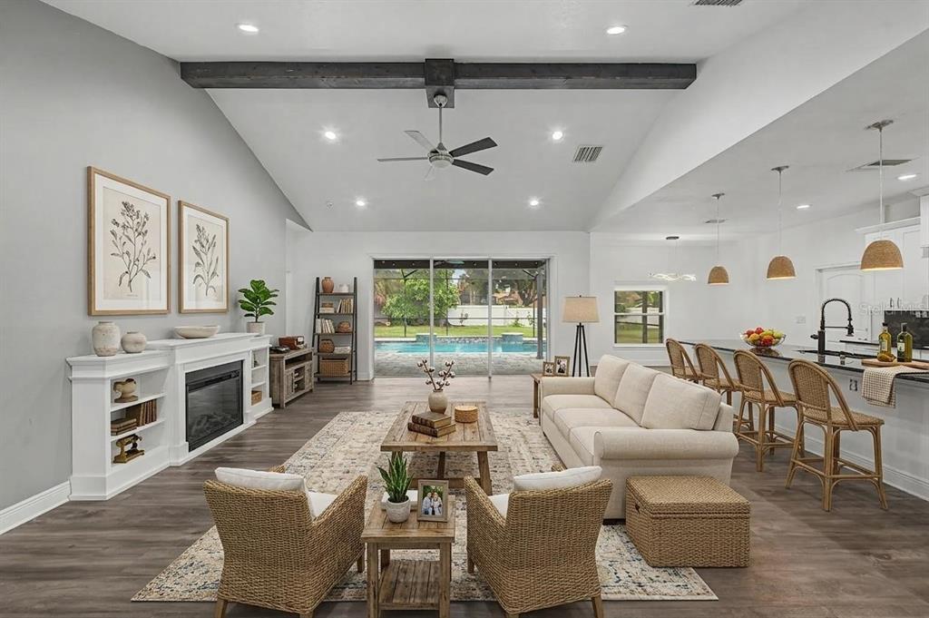 An open-concept living room features a fireplace, vaulted ceiling, and a view of a pool — 606 ROYAL CREST DRIVE, BRANDON, FL