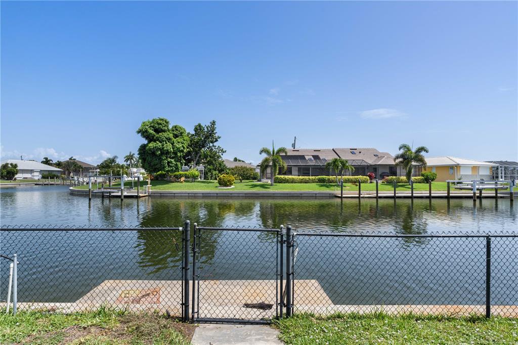 A fenced concrete dock overlooks a canal with houses and palm trees in the background — 2208 CASSINO COURT, PUNTA GORDA, FL