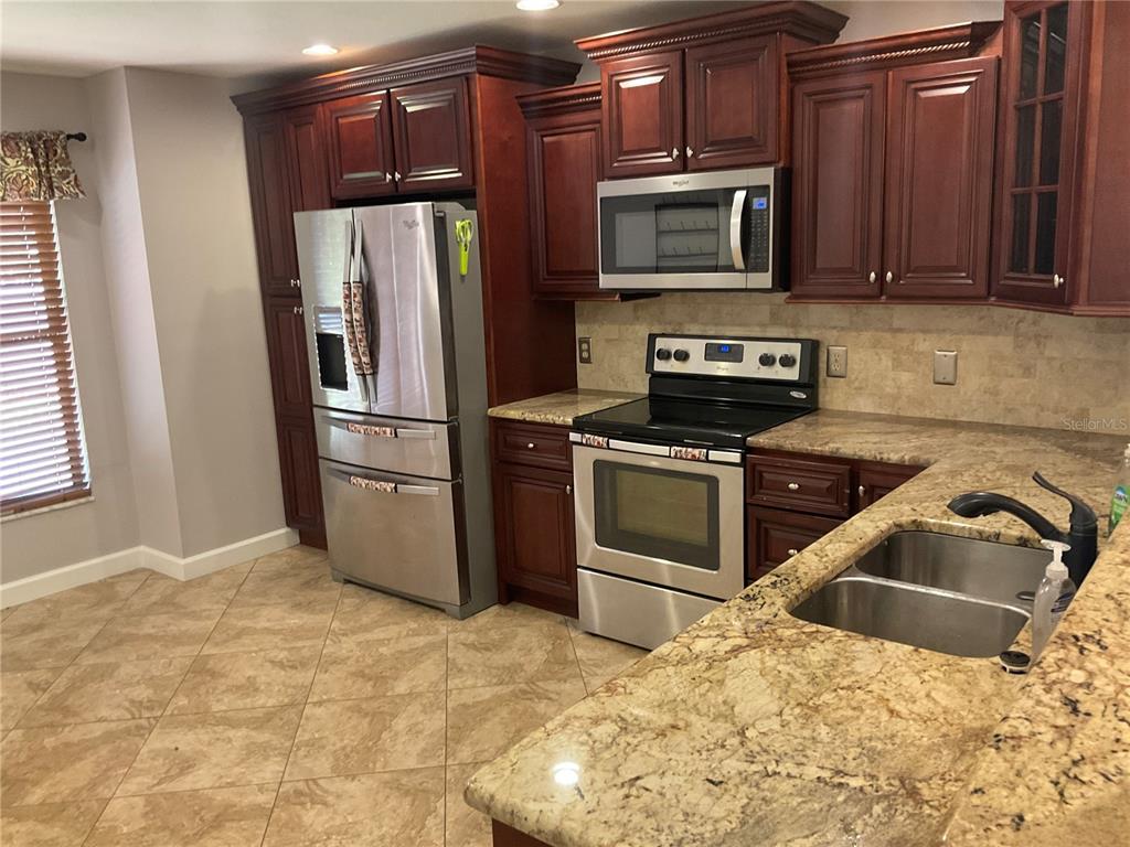 A kitchen features dark wood cabinets, granite countertops, stainless steel appliances, and tiled flooring — 4273 STAFFORD DRIVE, WINTER HAVEN, FL