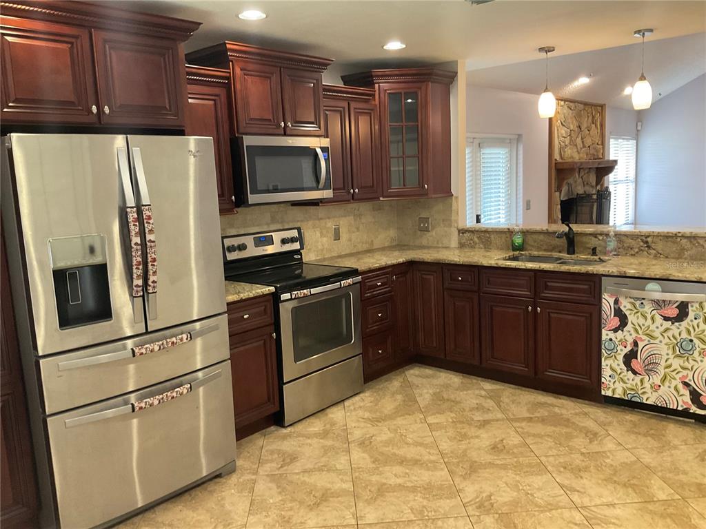 A kitchen with dark wood cabinets, stainless steel appliances, and a patterned dishwasher cover — 4273 STAFFORD DRIVE, WINTER HAVEN, FL