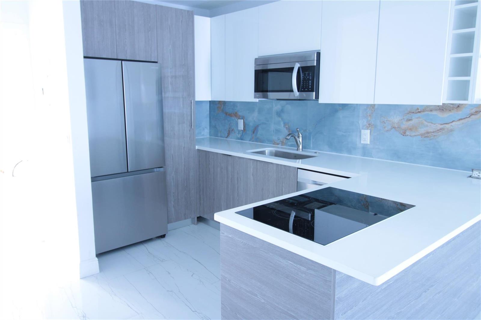 A modern kitchen features wood-grain cabinets, white countertops, a blue marble backsplash, and stainless appliances — 600 Layne Boulevard # 119, Hallandale Beach FL 33009, HALLANDALE BEACH, FL