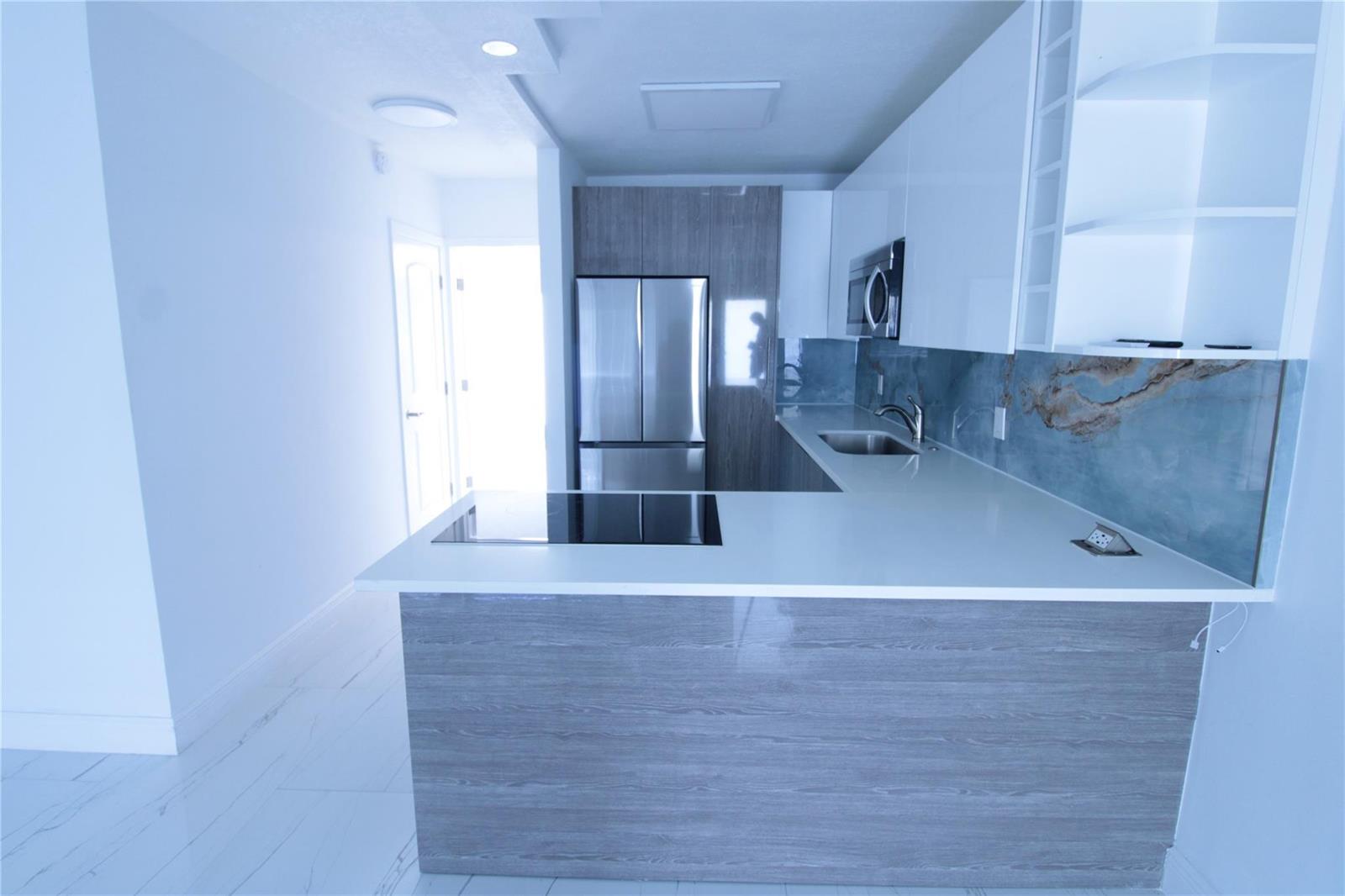 A modern kitchen features white cabinets, a wood-grain island, stainless steel appliances, and blue backsplash — 600 Layne Boulevard # 119, Hallandale Beach FL 33009, HALLANDALE BEACH, FL