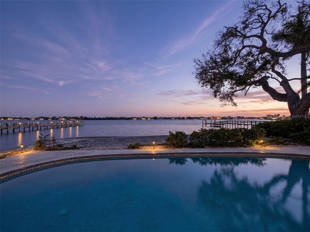 A swimming pool overlooks a waterfront view with a large tree and two wooden docks — 1267 STARBOARD LANE, SARASOTA, FL