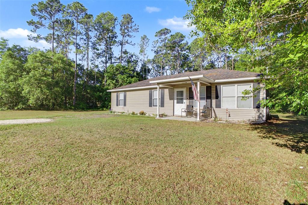 A single-story tan house with a covered front porch sits on a grassy lot — 1886 LAUREL AVENUE, BUNNELL, FL