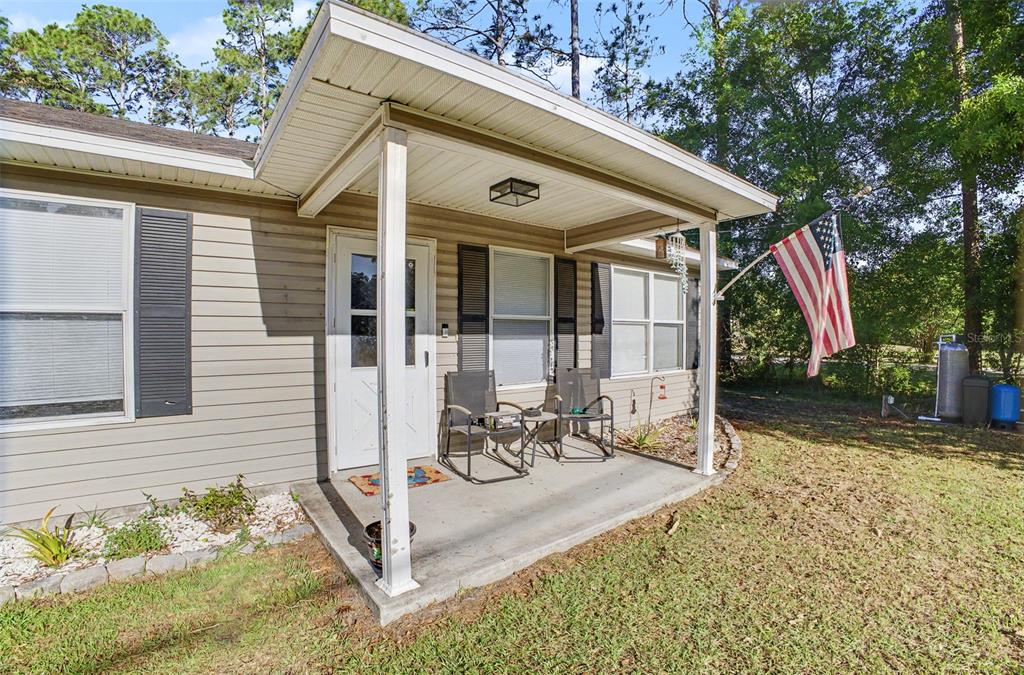 A tan house exterior features a covered front porch with two chairs and a flag — 1886 LAUREL AVENUE, BUNNELL, FL