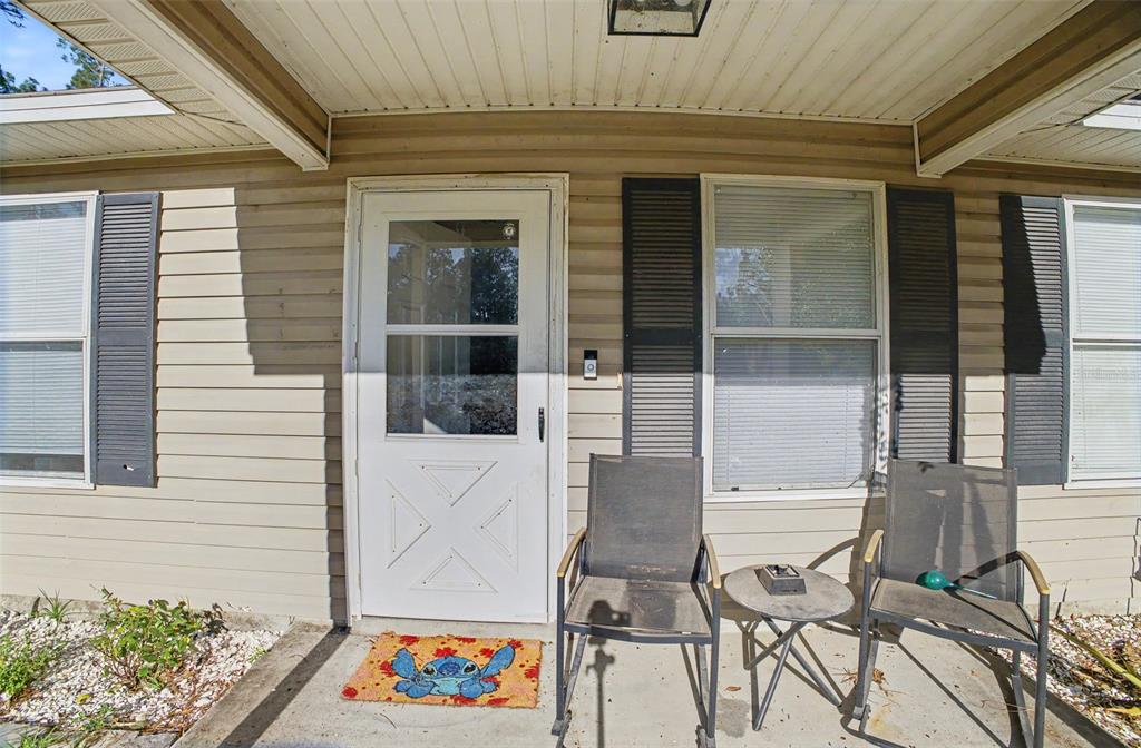 A beige-sided house exterior features a white storm door, two chairs, and a small table — 1886 LAUREL AVENUE, BUNNELL, FL