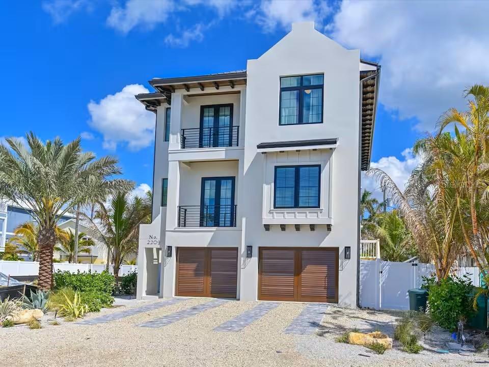 A three-story white house with a gravel driveway, two garage doors, and two balconies — 2209 AVENUE B, BRADENTON BEACH, FL