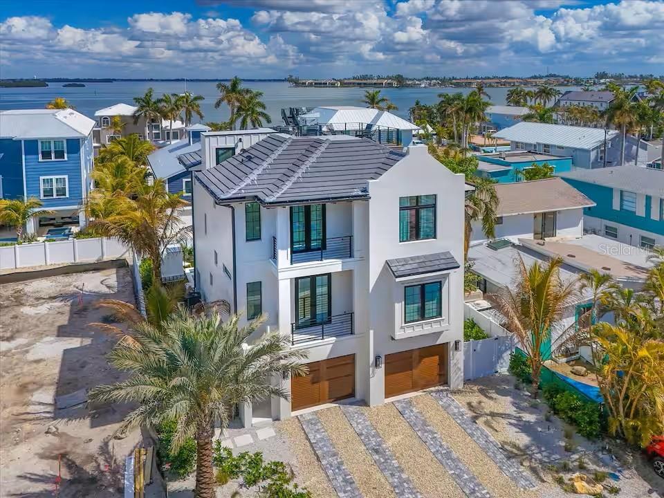 An elevated three-story white house with a dark tiled roof and two wooden garage doors — 2209 AVENUE B, BRADENTON BEACH, FL