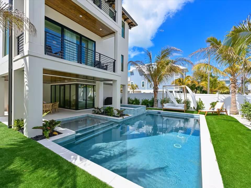 A modern multi-story house features a swimming pool, covered patio, and artificial turf lawn — 2209 AVENUE B, BRADENTON BEACH, FL
