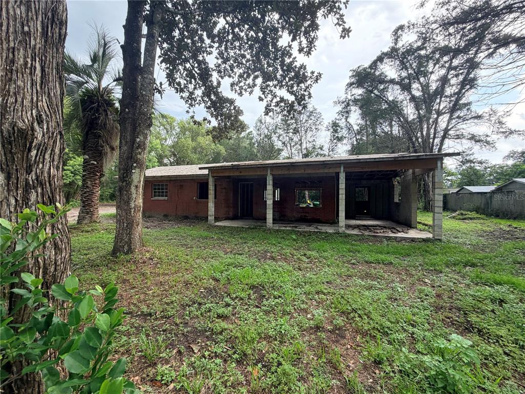 A single-story brick house with a covered porch sits on a grassy, tree-filled lot — 343 LINCOLN AVENUE, BROOKSVILLE, FL