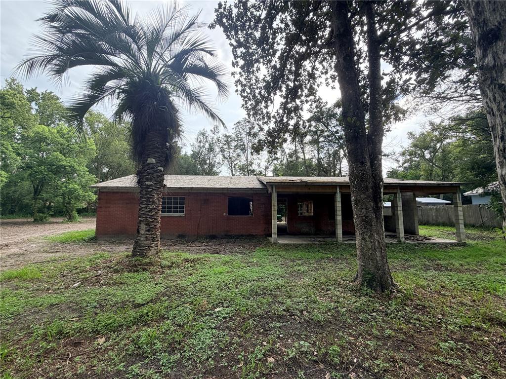 A single-story brick house with a covered front porch sits on a grassy, wooded lot — 343 LINCOLN AVENUE, BROOKSVILLE, FL