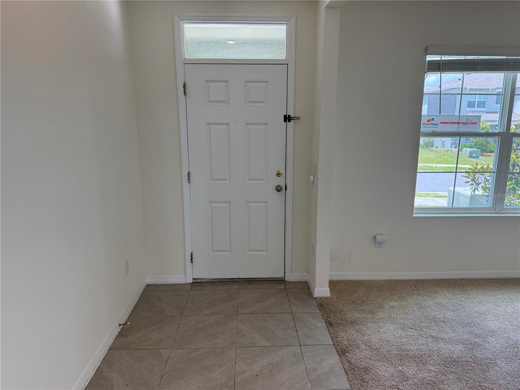 A white front door with a transom window opens into a tiled entryway with carpeted flooring — 2029 MAPLE RIDGE DRIVE, ZELLWOOD, FL