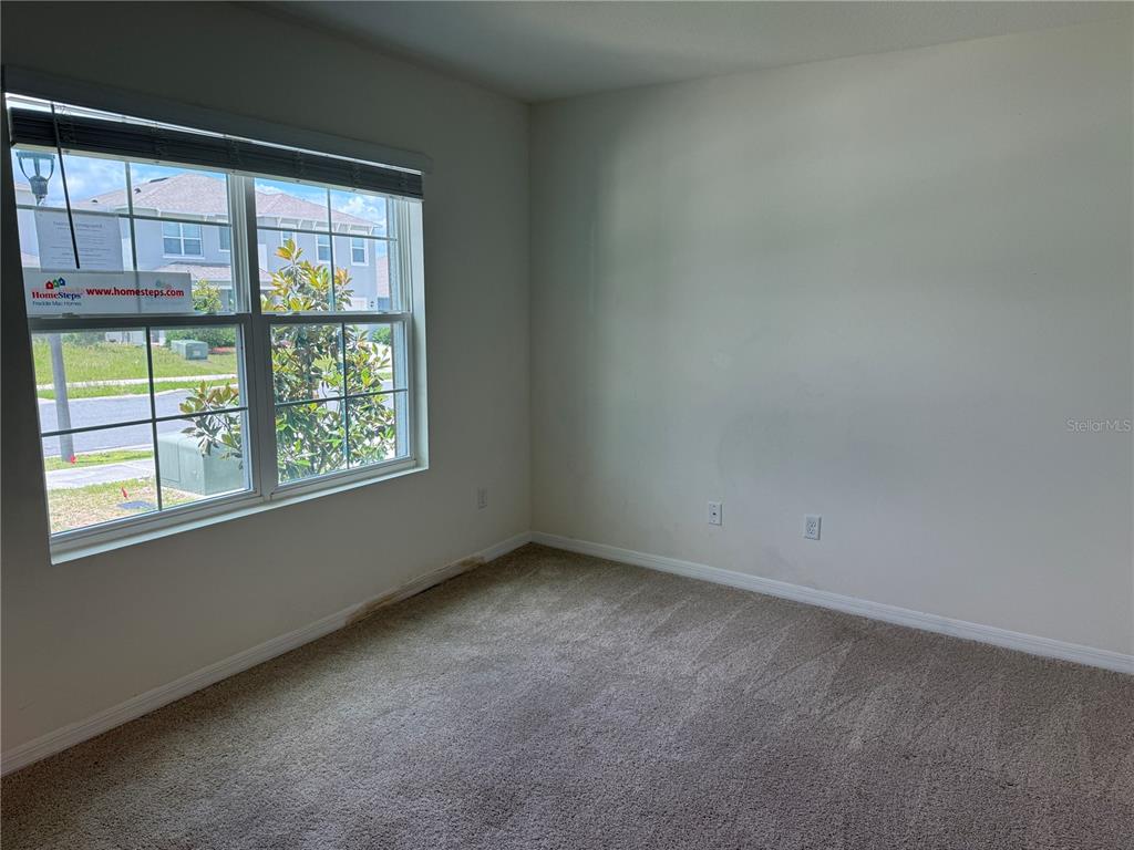 An empty bedroom with beige carpet, white walls, and a window overlooking a suburban street — 2029 MAPLE RIDGE DRIVE, ZELLWOOD, FL