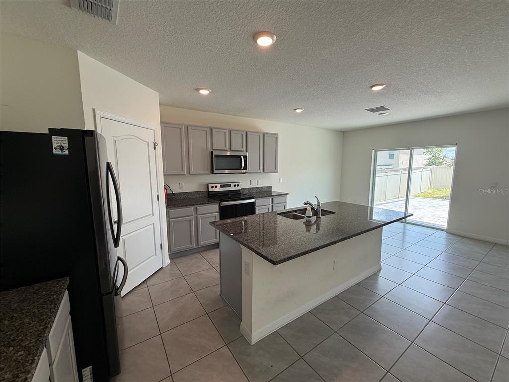 A kitchen features gray cabinets, dark granite countertops, a center island, and tile flooring — 2029 MAPLE RIDGE DRIVE, ZELLWOOD, FL