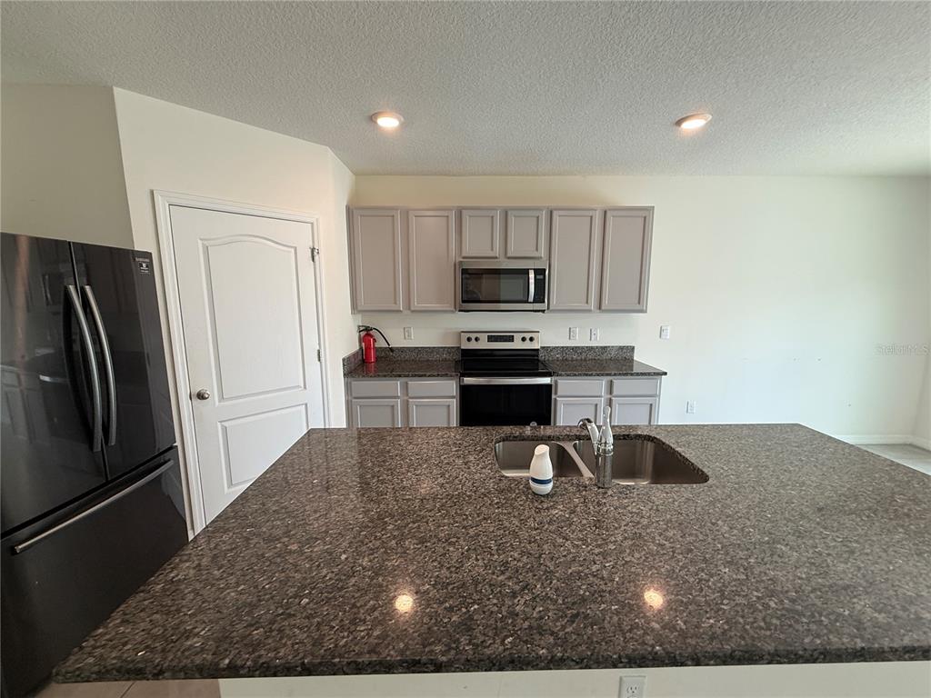 A kitchen features gray cabinets, granite countertops, a stainless steel microwave, and a center island — 2029 MAPLE RIDGE DRIVE, ZELLWOOD, FL