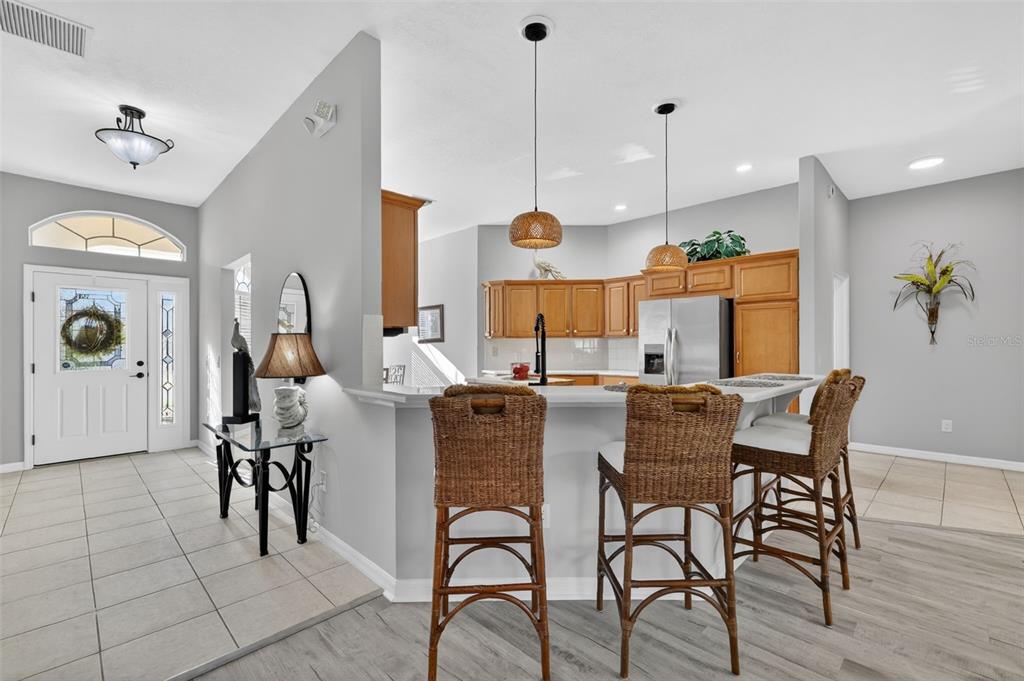 A kitchen with wood cabinets and a breakfast bar overlooks a tiled entryway — 17325 SE 73RD PARK GLEN COURT, THE VILLAGES, FL