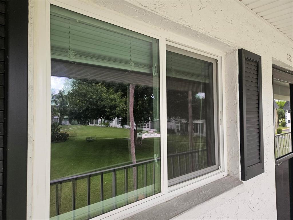 A white-framed window with black shutters on a textured exterior wall overlooking a grassy lawn — 303 47TH AVENUE DR W UNIT 352, BRADENTON, FL
