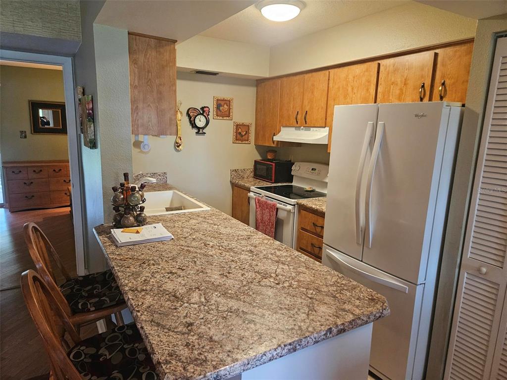 A kitchen features wood cabinets, granite countertops, a white refrigerator, and a breakfast bar — 303 47TH AVENUE DR W UNIT 352, BRADENTON, FL
