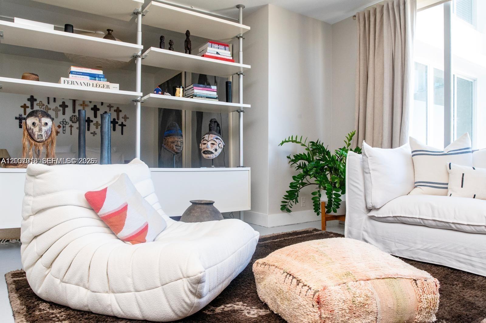 A living room features a white tufted lounge chair, a sofa, and open shelving with masks — 1000 West Ave # 1504, Miami Beach FL 33139, MIAMI BEACH, FL