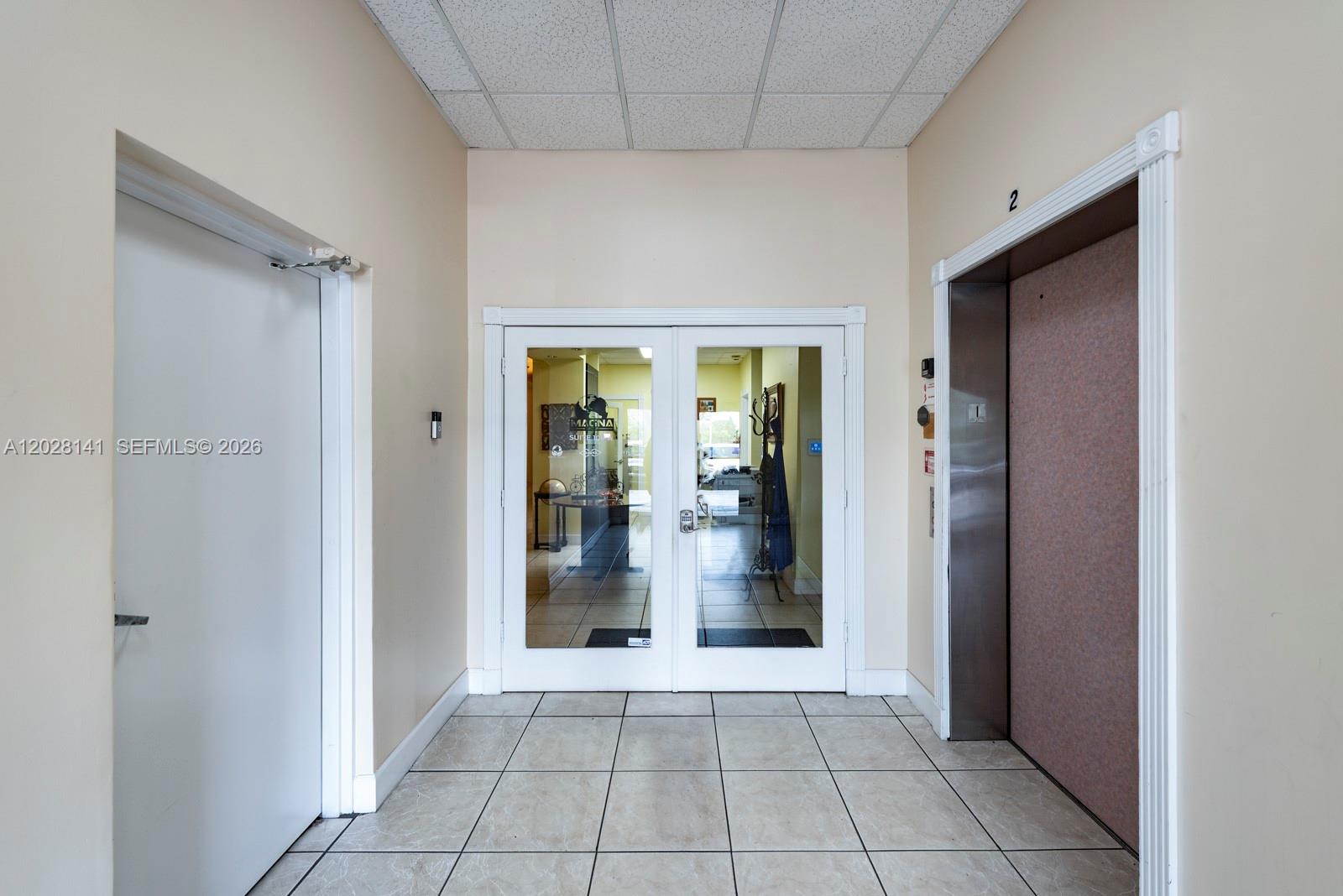 A tiled hallway features a white door, double glass entry doors, and an elevator — 10200 NW 25th St # A105, Doral FL 33172, DORAL, FL