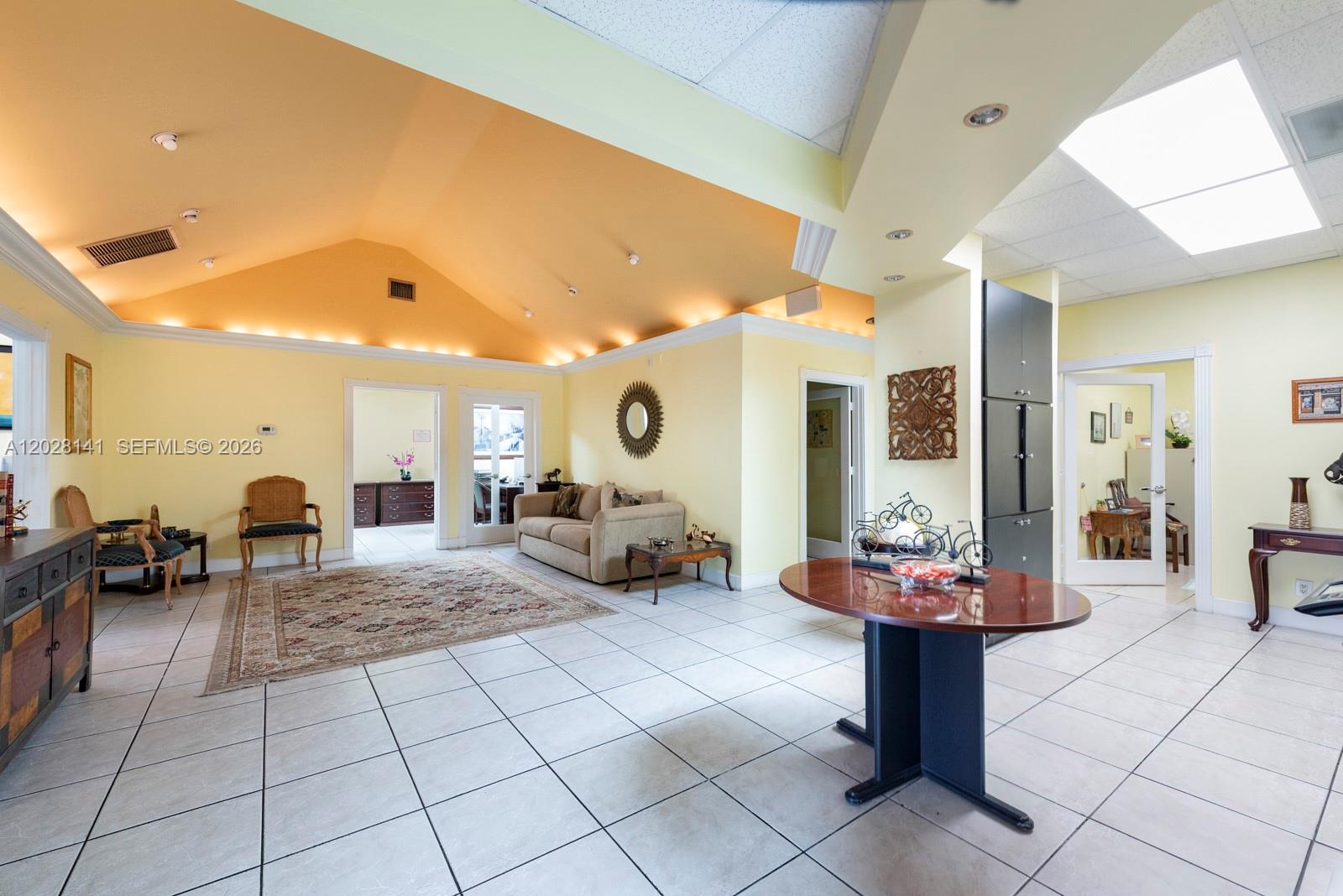 A spacious room with a vaulted yellow ceiling, tiled floors, and multiple doorways — 10200 NW 25th St # A105, Doral FL 33172, DORAL, FL