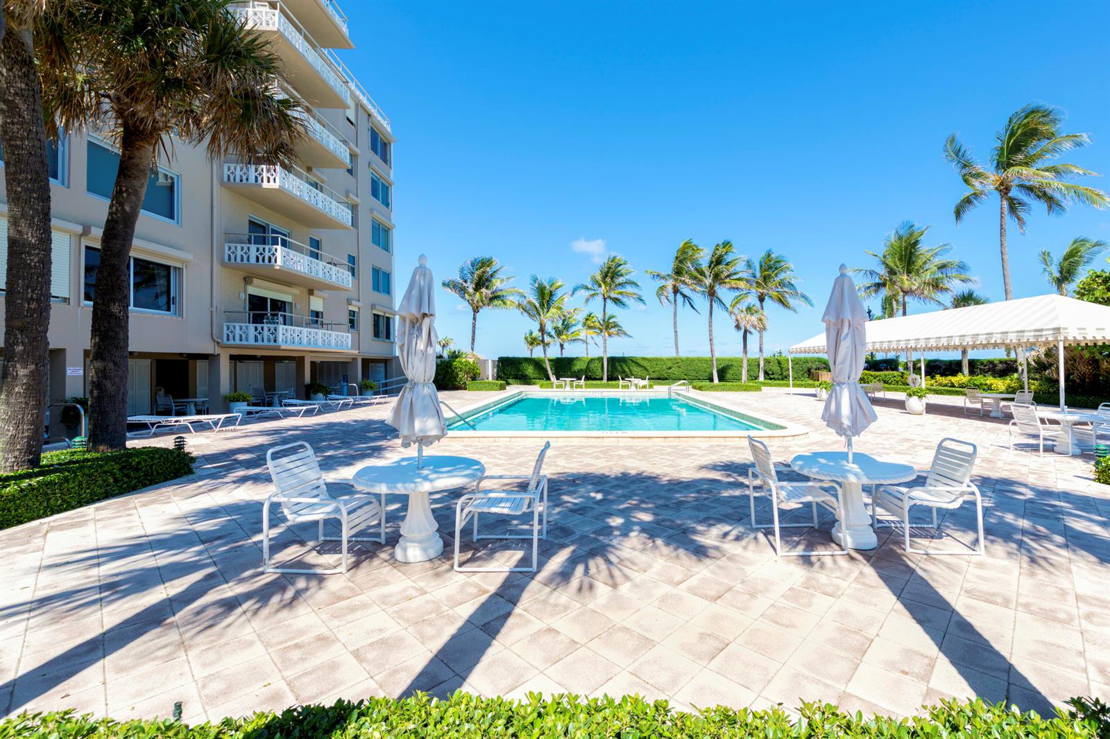 A swimming pool sits on a paved patio beside a multi-story building and palm trees — 139 Sunrise Avenue # 102, Palm Beach FL 33480, PALM BEACH, FL
