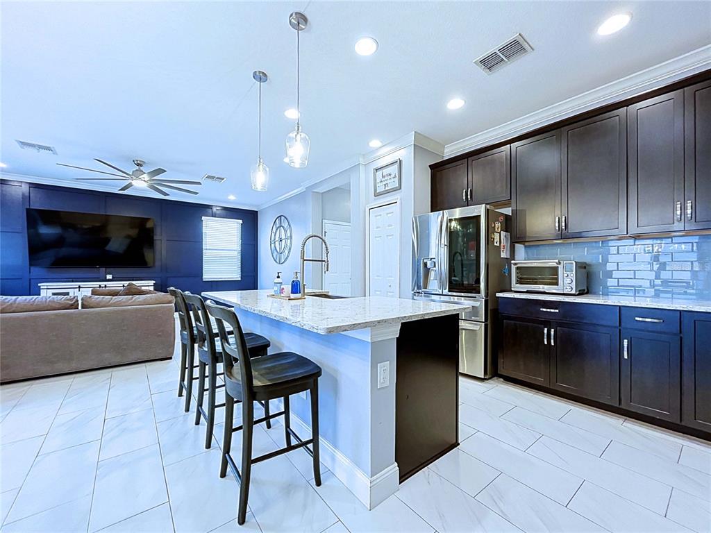 A kitchen with dark cabinets, a granite-topped island, and bar stools opens to a living area — 19219 LEONARD ROAD, LUTZ, FL
