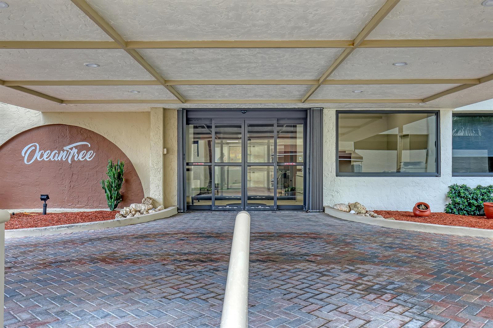 The entrance to the OceanTree building features a covered driveway, brick pavers, and sliding glass doors — 3400 N Ocean Drive # 101, Singer Island FL 33404, SINGER ISLAND, FL