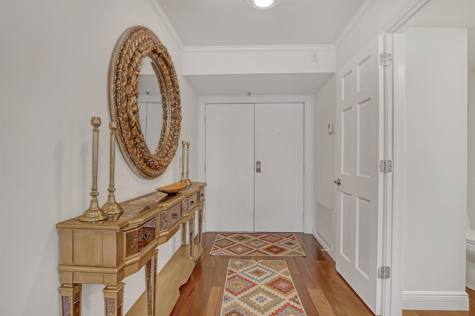 A hallway features a gold console table, a decorative mirror, and patterned rugs on wood floors — 3400 N Ocean Drive # 101, Singer Island FL 33404, SINGER ISLAND, FL