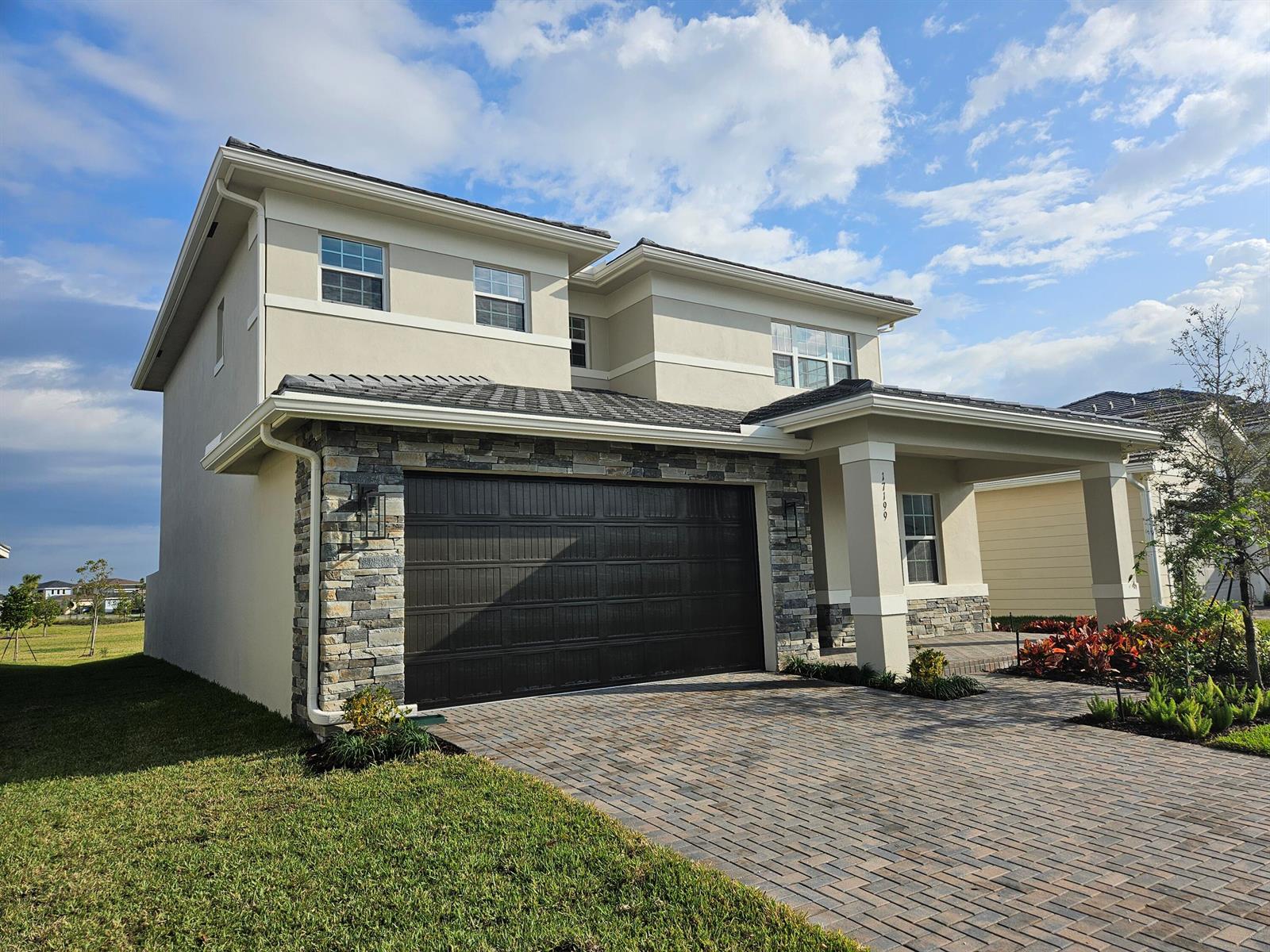 A two-story house with a stone-accented garage, a paved driveway, and a covered entryway — 17199 Tawny Owl Trail, FL 33470, FL